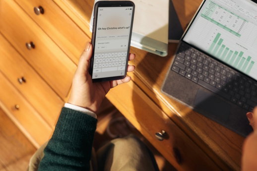 Person holding phone near laptop and tablet on desk
